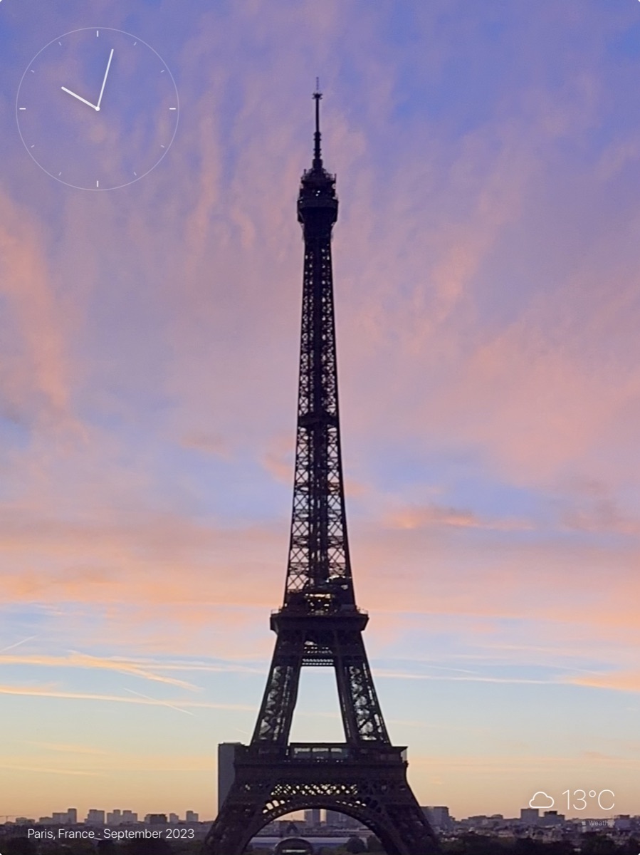 The Eiffel Tower in silhouette against a dusk sky, shown on an iPad held upright, with an analogue clock in the corner.